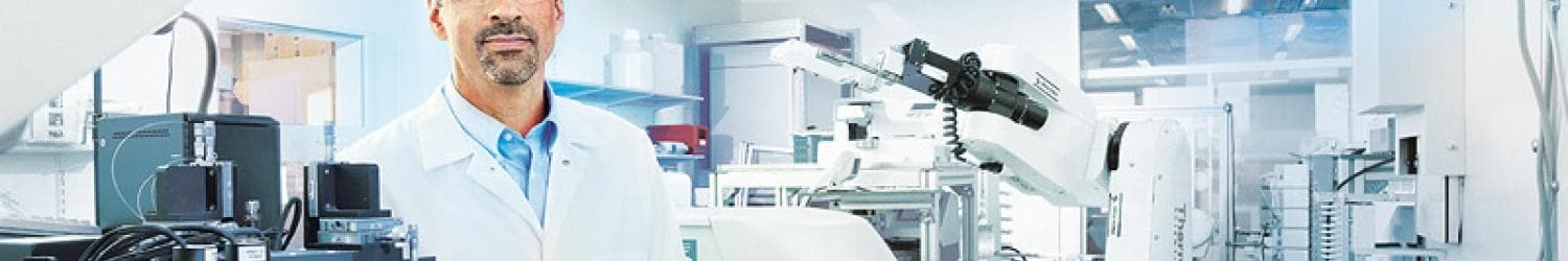 A scientist in a lab coat stands next to laboratory equipment and robotic machinery in a modern laboratory setting.