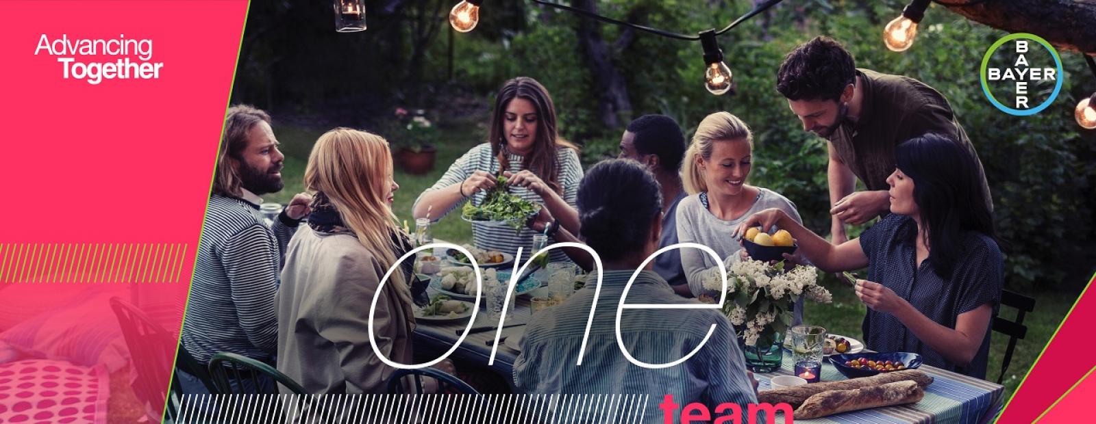 A group of people sitting around a table outdoors, sharing a meal. Text overlay reads "one team" with branding elements related to Bayer.