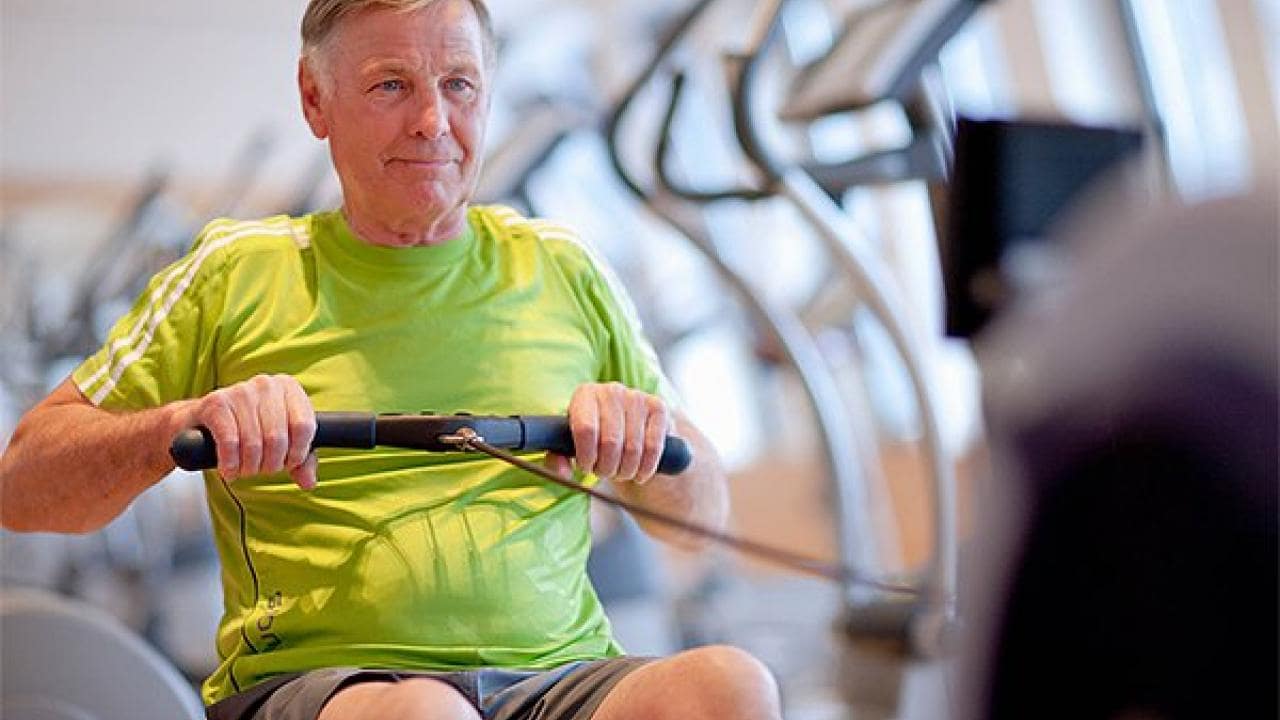 Older man in a bright green shirt using a rowing machine in a gym.