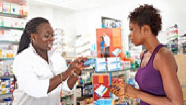 A pharmacist explains medication details to a customer in a pharmacy setting.