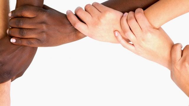 Hands of diverse skin tones interlocking in a circle against a white background, symbolizing unity and teamwork.