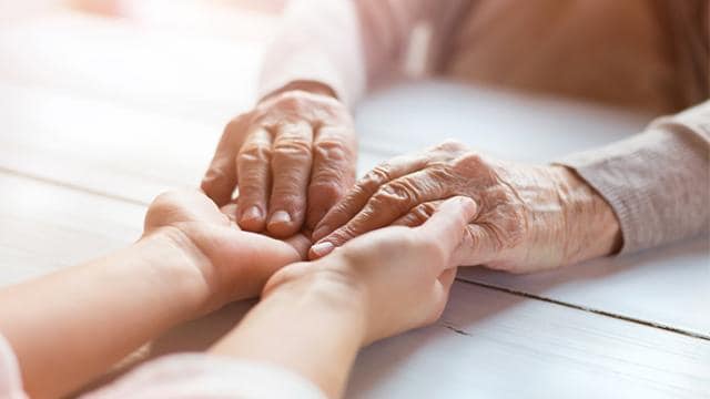 An elderly person's hands placed on top of a younger person's hands on a white wooden table.