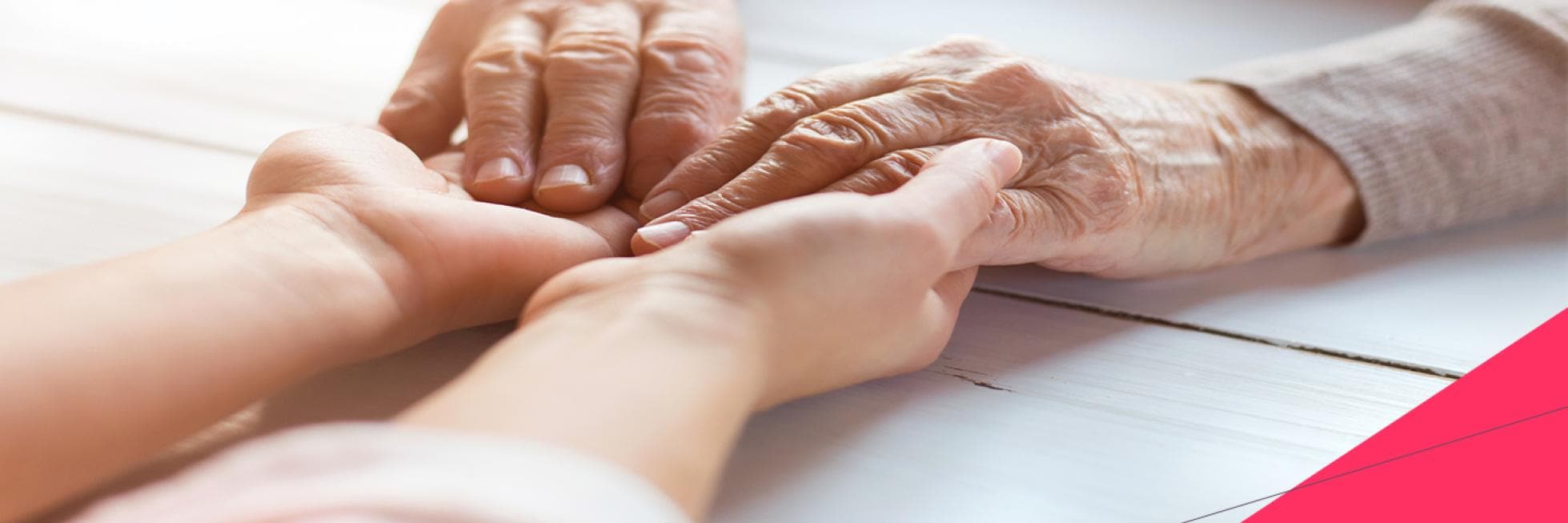 An elderly person's hands gently holding a younger person's hands on a white wooden surface.