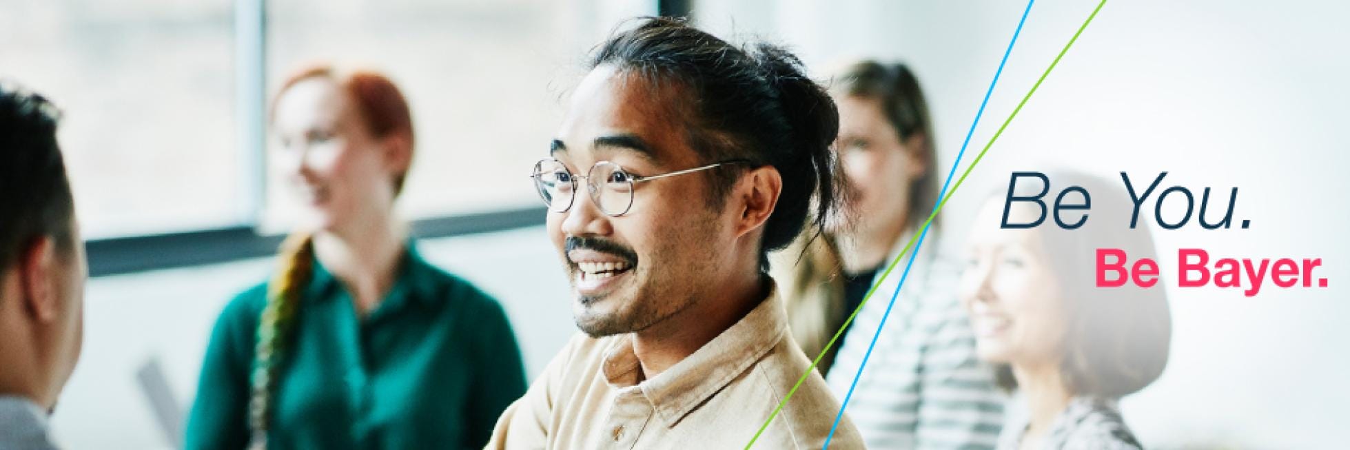 Diverse group of people smiling and talking in an office setting with the text "Be You. Be Bayer.